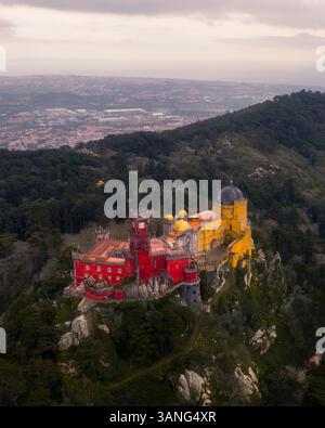 Blick aus der Vogelperspektive auf die farbenfrohe Burg Palacio da Pena auf einem Berg, umgeben von Wald, Sintra, Portugal. Stockfoto