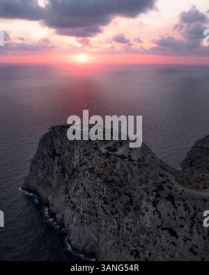 Blick aus der Vogelperspektive auf einen majestätischen Leuchtturm auf einer zerklüfteten Klippe mit Blick auf das ruhige Meer bei Sonnenaufgang, Cap de Formentor, Mallorca, Spanien. Stockfoto