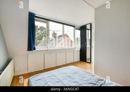 Ein geräumiges Schlafzimmer mit großen Fenstern bietet eine helle und luftige Atmosphäre. Das minimalistische Design mit gemütlicher Atmosphäre ist perfekt zum Entspannen. Stockfoto