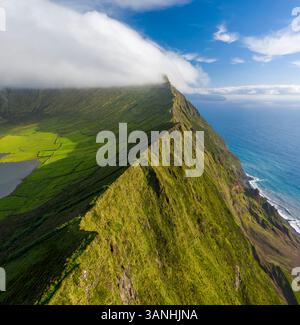 Aus der Vogelperspektive auf einen scharfen Bergrücken entlang der Küste mit Blick auf das Meer auf der Insel Corvo, Azoren, Portugal. Stockfoto