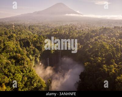 Blick aus der Vogelperspektive auf den Coban Sewu Wasserfall umgeben von Waldbäumen mit dem vulkanischen Berg Semeru im Hintergrund, Ost-Java, Indonesien. Stockfoto