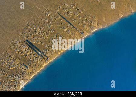 Aus der Vogelperspektive auf Fischer, die während des Sonnenaufgangs am Ufer angeln, wenn der Sand Gold ist und das Wasser des Flusses glatt wie Seide ist, in Ria de Aveiro, Tor Stockfoto