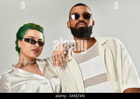 Ein stilvolles Paar posiert selbstbewusst in einem Studio mit einzigartigen Outfits und trendigen Sonnenbrillen. Stockfoto