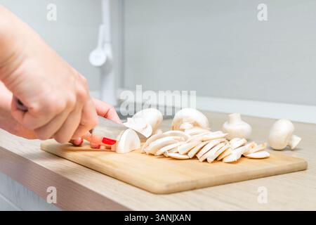 Frau, die Pilze auf Holzbrett in der Küche schneidet. Hausfrau schneidet Champignonpilze. Pilze zuhause kochen. Pilze in der Küche Stockfoto