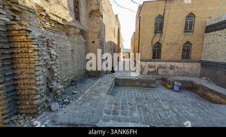 Eine enge Gasse zwischen alten Ziegelgebäuden mit Bogenfenstern, mit einem kleinen Innenhof mit Steinpflaster und verstreuten Trümmern. Stockfoto