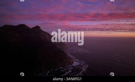Aus der Vogelperspektive auf die Silhouette des Sonnenuntergangs über der Küstenlandschaft mit felsigen Klippen und dem Meer, Chapmans Peak, Kapstadt, Westkap, Südafrika. Stockfoto