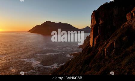 Aus der Vogelperspektive auf den Sonnenuntergang an der Küste mit Wellen und majestätischen Bergen, Chapmans Peak, Western Cape, Südafrika. Stockfoto