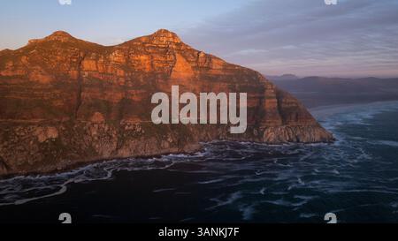 Aus der Vogelperspektive auf den majestätischen Chapmans Peak mit zerklüfteten Klippen und ruhigen Meereswellen bei Sonnenuntergang, Kapstadt, Westkap, Südafrika. Stockfoto