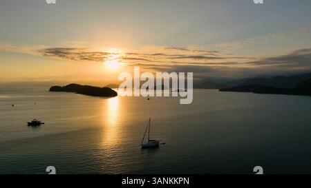 Blick aus der Vogelperspektive auf den tropischen Sonnenuntergang über einem ruhigen Archipel mit Segelbooten und Wolken, Paraty, Brasilien. Stockfoto