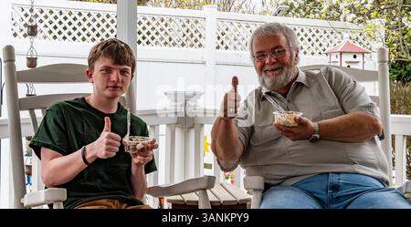 Zwei Familienmitglieder entspannen sich im Frühjahr auf einer Veranda und teilen sich Eisspezialitäten. Der Großvater und der Enkel lächeln und zeigen die Daumen hoch, was eine fröhliche Mome erschafft Stockfoto