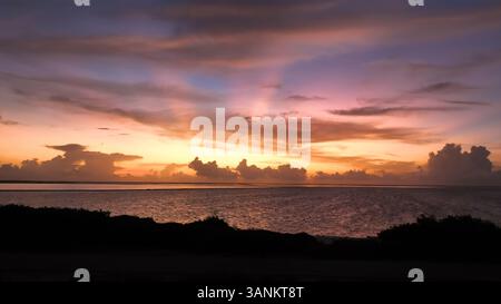 Blick aus der Vogelperspektive auf die ruhige tropische Insel bei Sonnenaufgang mit lebendigem Meer und farbenfrohem Himmel, Karibik Niederlande. Stockfoto