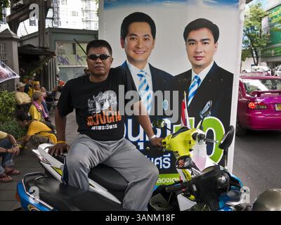 22. Juni 2011 - Bangkok, Thailand - Ein Mann sitzt auf seinem Motorrad vor einem Wahlkampfplakat für den amtierenden thailändischen Premierminister Abhisiti Vejjajiva am Mittwoch in Bangkok. Yingluck Shinawatra, Führer der Pheua Thai Partei, kandidiert gegen den amtierenden Premierminister Abhisit Vejjajiva, den Vorsitzenden der Demokratischen Partei. Yingluck ist die jüngste Schwester des ehemaligen Premierministers Thaksin Shinawatra, der 2006 durch einen Militärputsch abgesetzt wurde. Yingluck ist derzeit führend in Meinungsumfragen und ist der Demokratischen Partei weit voraus, die Thailand in der einen oder anderen Form den größten Teil des letzten 60 Jahres regiert hat Stockfoto