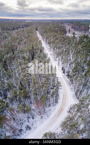 Aus der Vogelperspektive einer leeren, schneebedeckten Straße im Wald in Estland. Stockfoto