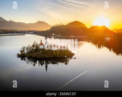 Blick aus der Vogelperspektive auf die Insel Bled bei Sonnenaufgang mit einer ruhigen Kirche und einem ruhigen See, umgeben von Bergen, Bled, Slowenien. Stockfoto