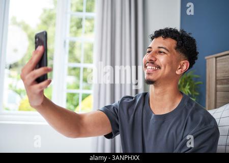 Junger lächelnder Mann, der drinnen ein Selfie mit natürlichem Licht macht Stockfoto
