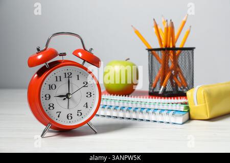 Wecker, Schreibwaren und Apfel auf weißem Holztisch. Zeit für Wissen Stockfoto