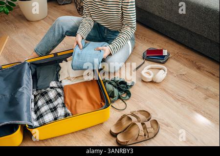 Junge Reisende, die auf dem Boden sitzt und Koffer packt, bereitet sich auf die Sommerferien vor... Stockfoto
