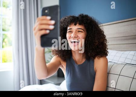Junge Frau mit lockigem Haar lächelt, während sie zu Hause ein Selfie macht Stockfoto