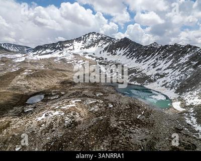 Aus der Vogelperspektive auf atemberaubende schneebedeckte Berge und ruhige Seen unter einem dramatischen Himmel, Deosai Nationalpark, Skardu, Pakistan. Stockfoto