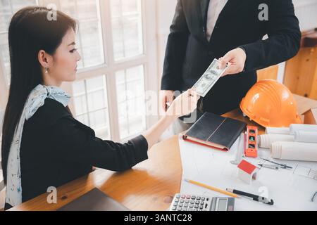Ein Mann, der einer Architektin hunderte Dollar-Scheine anbietet. Geschäftsmann gibt seinem Partner Geld. Frau, die Geld vom Geschäftsmann erhält. Venal Stockfoto