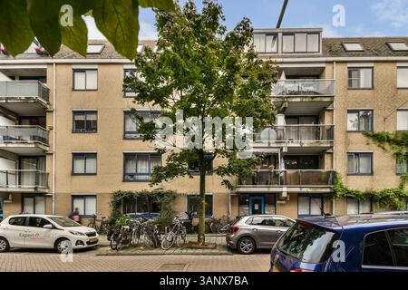 Ein zeitgenössischer Apartmentkomplex mit mehreren Balkonen, umgeben von geparkten Fahrrädern und Autos, zeigt urbanes Leben in einem lebendigen Viertel. Stockfoto