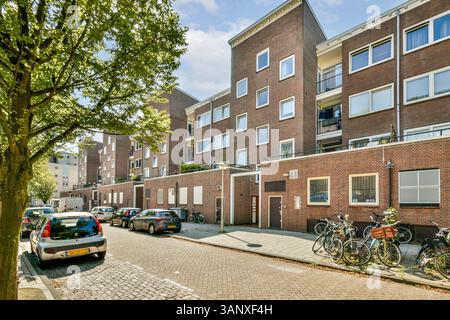 Eine lebhafte Straße mit modernen Wohngebäuden mit geparkten Autos und Fahrrädern, umgeben von üppigem Grün und einem klaren blauen Himmel. Stockfoto