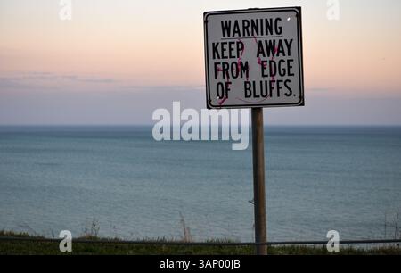 Ein Warnschild, um sich von einer Klippe über dem Ontario-See fernzuhalten, unter einem Abendhimmel Stockfoto