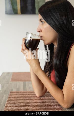 Nach dem Abkühlen ihres Kaffees nimmt eine junge Frau einen behutsamen Schluck und genießt die Wärme in einem friedlichen und intimen Moment ihrer Morgenroutine. Stockfoto