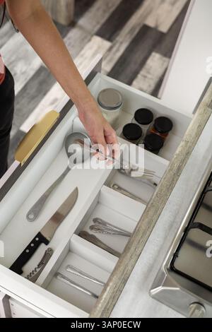 In der offenen Küchenschublade finden Sie ordentlich organisierte Utensilien – Löffel, Schöpflöffel, Messer, Gabeln und mehr – in einem eleganten, modernen Holzschrank. Stockfoto