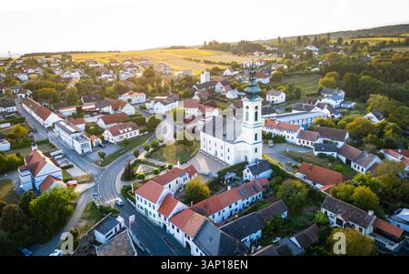 Blick aus der Vogelperspektive auf das malerische Dorf mit traditioneller Kirche und charmanten Häusern, umgeben von lebhaften Feldern und Grün, Stadtschlaining, Österreich. Stockfoto