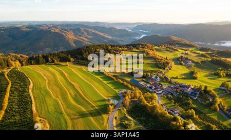 Blick aus der Vogelperspektive auf den ruhigen Sonnenaufgang über wunderschönem Ackerland und sanften Hügeln, Oberndorf, Österreich. Stockfoto