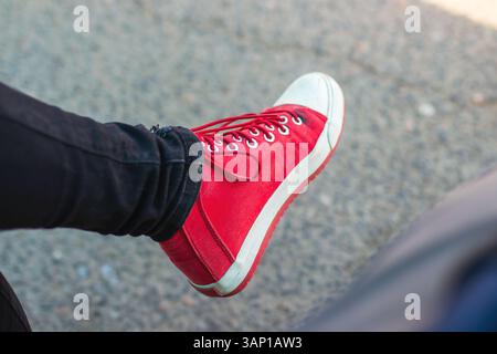 Dieses Bild zeigt eine Nahaufnahme des Fußes einer Person, die stilvolle rote Sneakers trägt, mit leuchtenden Farben und modischem Design Stockfoto