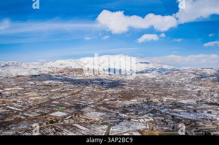 Luftaufnahme eines Tals mit landwirtschaftlichem Feld im Winter mit Schnee und Berg im Hintergrund, Golanhöhen, Israel. Stockfoto