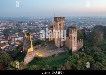 Blick aus der Vogelperspektive auf die Burg scaligero und borghetto mit italienischer Flagge bei einem wunderschönen Sonnenuntergang, Valeggio sul Mincio, Italien. Stockfoto
