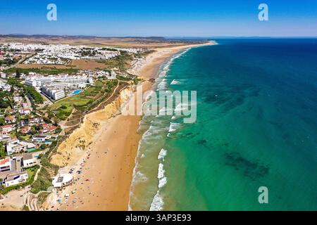 Aus der Vogelperspektive auf eine Küste mit Klippen, entlang der Linie von weißen Wellen und türkisfarbenem Wasser in der Stadt Conil de la Frontera an der Playa La Fontanilla in Cádiz, Andalusien, Spanien. Stockfoto