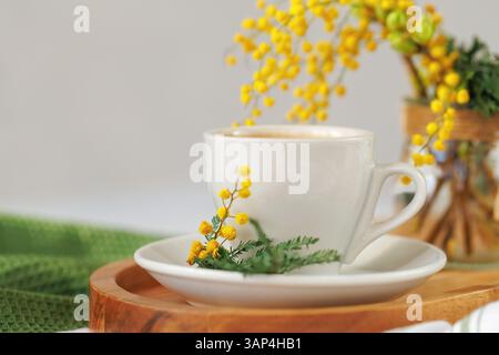 Frisch gebrühter Kaffee mit Mimosa-Blüten auf einem Holztablett Stockfoto