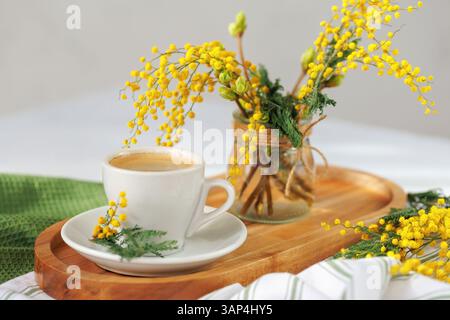 Weiße Tasse Kaffee mit Mimosa-Bouquet im Hintergrund Stockfoto