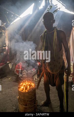 Porträt eines Mannes am heiligen Feuer, gekleidet in einem rituellen Kostüm aus getrockneten Palmblättern, nach einer ganztägigen Bwiti-Zeremonie. Stockfoto