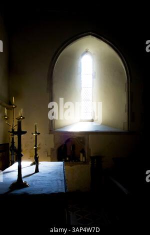 Das Licht, das durch ein bogenförmiges Kirchenfenster strömt, fällt auf Kirchenkerzen und Kerzenleuchter, das Licht schafft eine dramatische Atmosphäre Stockfoto