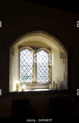 Licht strömt durch ein Kirchenfenster mit drei weißen Kerzen auf jeder Seite des Fensters auf dem Fenstervorsprung, über und unter dem Fenster die Wand i Stockfoto