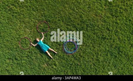 Aus der Vogelperspektive einer Frau, die mit Hula Hoop im öffentlichen Park in der Innenstadt von Zagreb, Kroatien, auf Gras liegt. Stockfoto