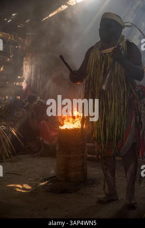 Porträt eines Mannes am heiligen Feuer, gekleidet in einem rituellen Kostüm aus getrockneten Palmblättern, nach einer ganztägigen Bwiti-Zeremonie. Stockfoto