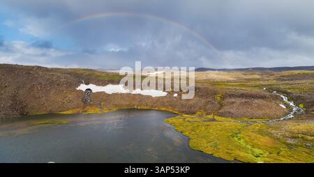 Panoramablick auf den Regenbogen über Bergplateau mit Wasserfall und Schneereste, Dynjandischeidi, Westfjorde, Island Stockfoto