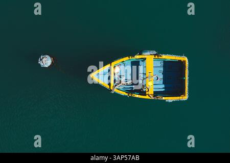 Von oben aus blickt man auf ein winziges, farbenfrohes Holzboot, das im Mittelmeer schwimmt, Malta. Stockfoto