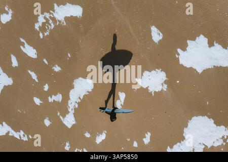 Aus der Vogelperspektive des Surfer-Schattens, der im Winter am Strand in Klaipeda, Litauen, spaziert. Stockfoto