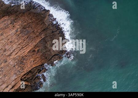 Blick aus der Vogelperspektive auf wunderschöne Klippen und zerklüftete Felsen entlang einer unberührten Küste mit türkisfarbenen Meereswellen, Algave, Portugal. Stockfoto
