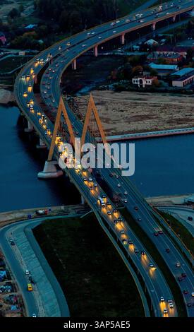 Blick aus der Vogelperspektive auf die tausendjährige Brücke über einen belebten Fluss mit moderner Stadtlandschaft und Abendlichtern, Kasan, Tatarstan Republik, Russland. Stockfoto
