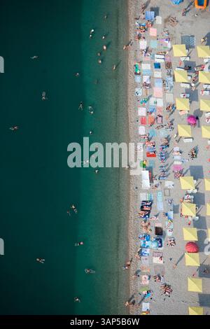 Aus der Vogelperspektive auf einen überfüllten Strand mit bunten Sonnenschirmen und Sonnenanbetern unter sonnigem Himmel, Koktebel, Russland. Stockfoto