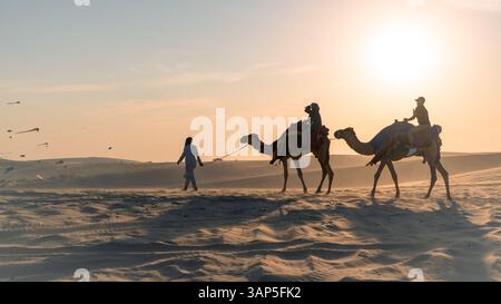 Doha, Katar, 24. Februar 2025: Eine Gruppe von Menschen, die auf Kamelen durch die goldenen Wüstendünen reiten, symbolisiert Ramadans spirituelle Reise und sein Erbe. Stockfoto