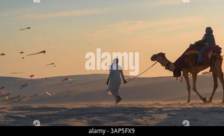 Doha, Katar, 24. Februar 2025: Eine Gruppe von Menschen, die auf Kamelen durch die goldenen Wüstendünen reiten, symbolisiert Ramadans spirituelle Reise und sein Erbe. Stockfoto